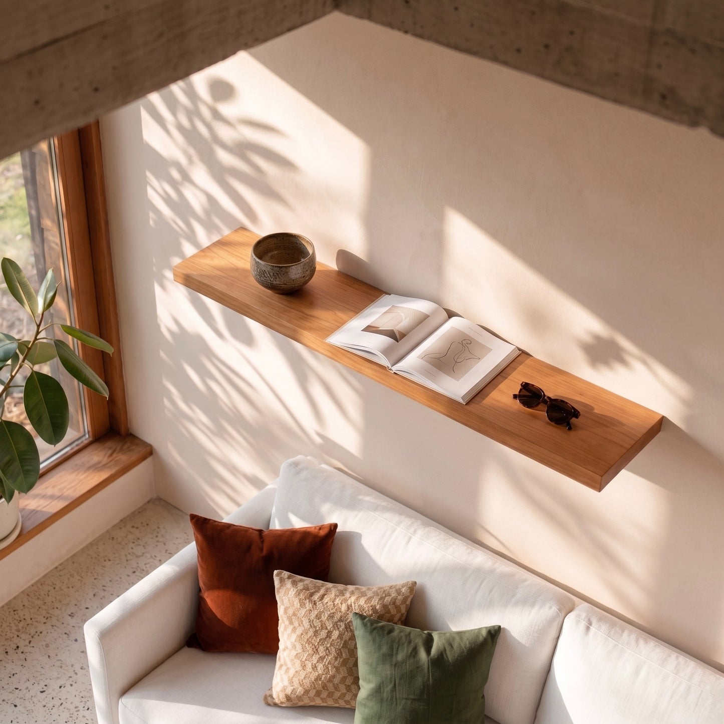 Schwebendes Wandregal aus Kirschbaum Massivholz über hellem Sofa mit Buch, Sonnenbrille und Keramikschale in modernem Japandi-Wohnzimmer bei warmem Sonnenlicht und großen Fenstern