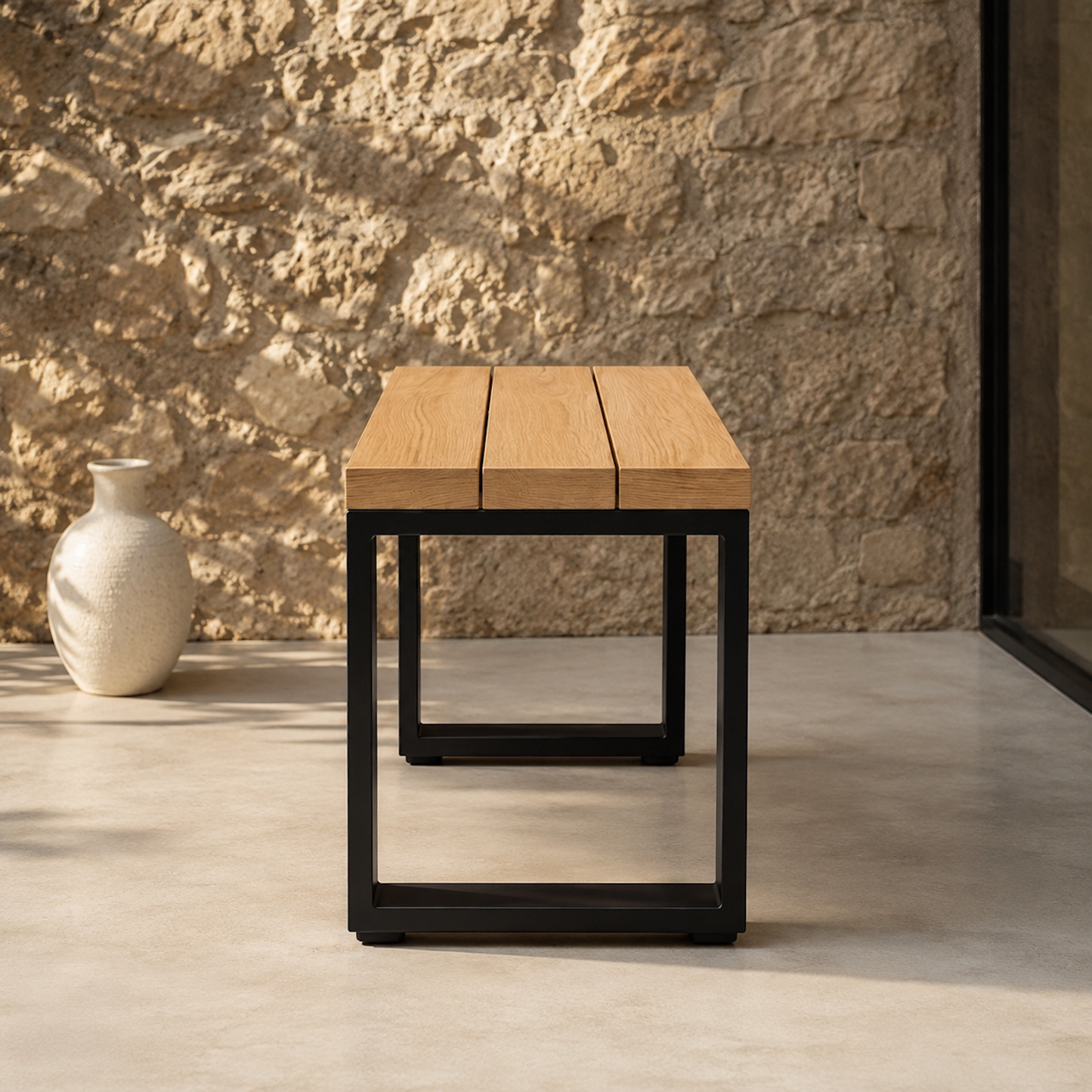 Frontal aufgenommenen Sitzhocker Urban aus massiver Eiche mit schwarzem Stahlgestell auf einer modernen Terrasse. Minimalistisches Outdoor-Design mit klaren Linien, heller Steinwand und warmem Sonnenlicht.