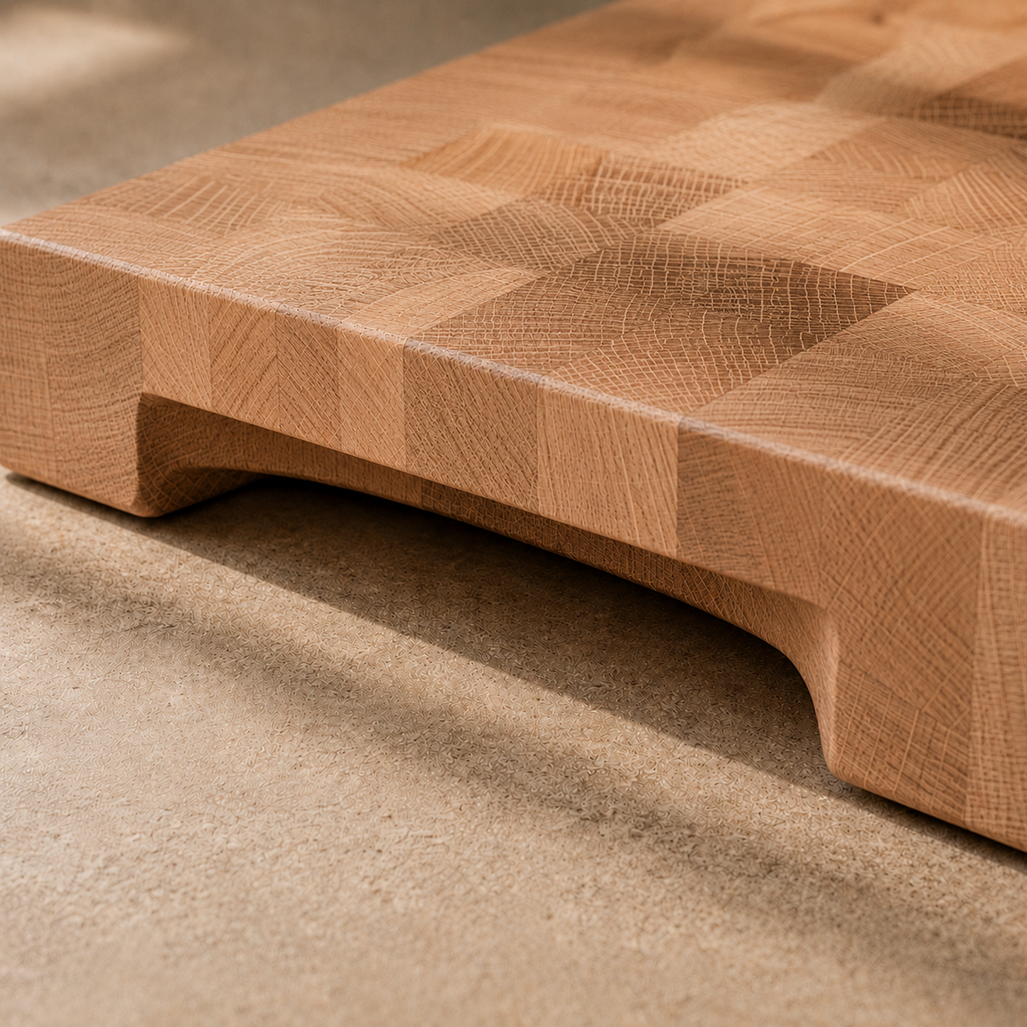 Nahaufnahme der integrierten Griffmulde eines Stirnholz-Schneidebretts aus Buche mit markanter Endgrain-Struktur und weichen Rundungen auf heller Steinoberfläche.