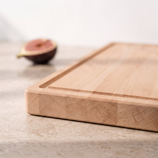 Nahaufnahme eines Schneidebretts aus Buche mit eingefräster Saftrille, massiver Holzkante und fein gemaserter Oberfläche.