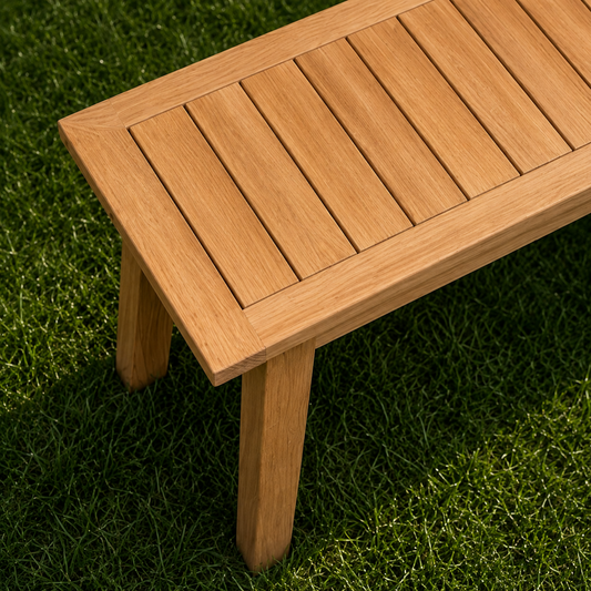 Detailaufnahme der Gartenbank Terra aus massiver Eiche mit Lamellen-Sitzfläche und schrägen Holzbeinen. Moderne Sitzbank aus Eichenholz mit natürlicher Holzmaserung auf grünem Rasen.