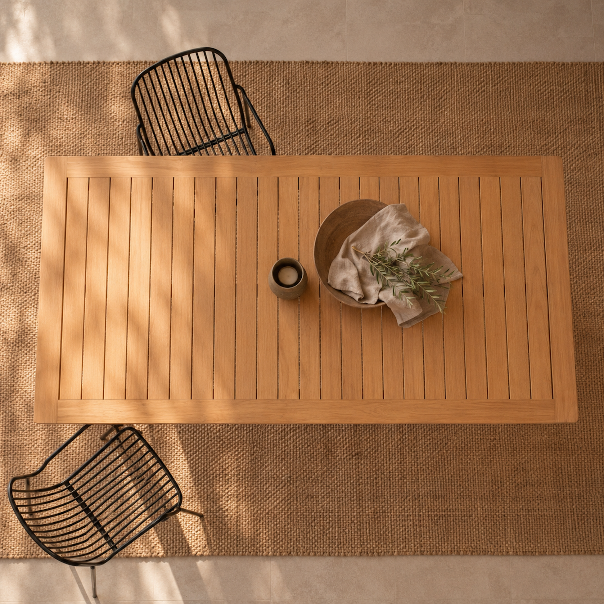 Draufsicht auf den Gartentisch Terra aus massiver Eiche mit rechteckiger Lamellen-Tischplatte. Moderner Outdoor-Esstisch aus Eichenholz auf gewebtem Teppich mit schwarzen Gartenstühlen im mediterranen Terrassenstil.