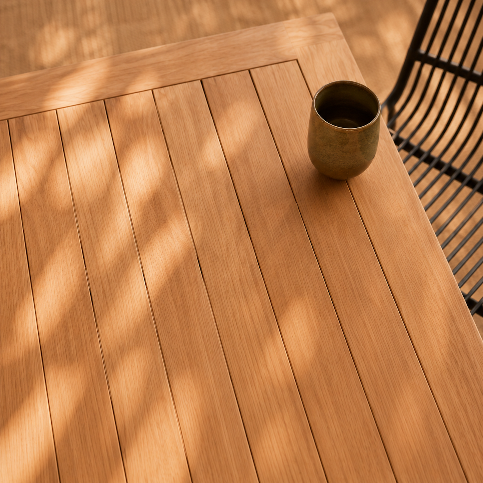 Detailaufnahme der Tischplatte des Gartentischs Terra aus massiver Eiche mit natürlicher Holzmaserung und Lamellen-Optik. Moderner Outdoor-Esstisch aus Eichenholz mit warmem Sonnenlicht auf mediterraner Terrasse.