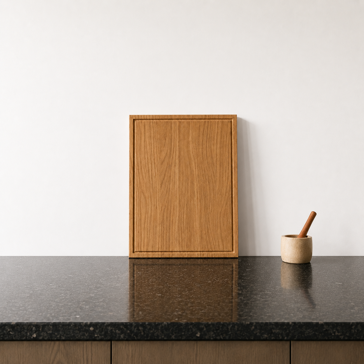 Massives Schneidebrett aus Eiche mit Saftrille auf dunkler Steinoberfläche vor heller Wand. Minimalistische Küchenszene mit natürlicher Holzmaserung und klarer Formsprache.