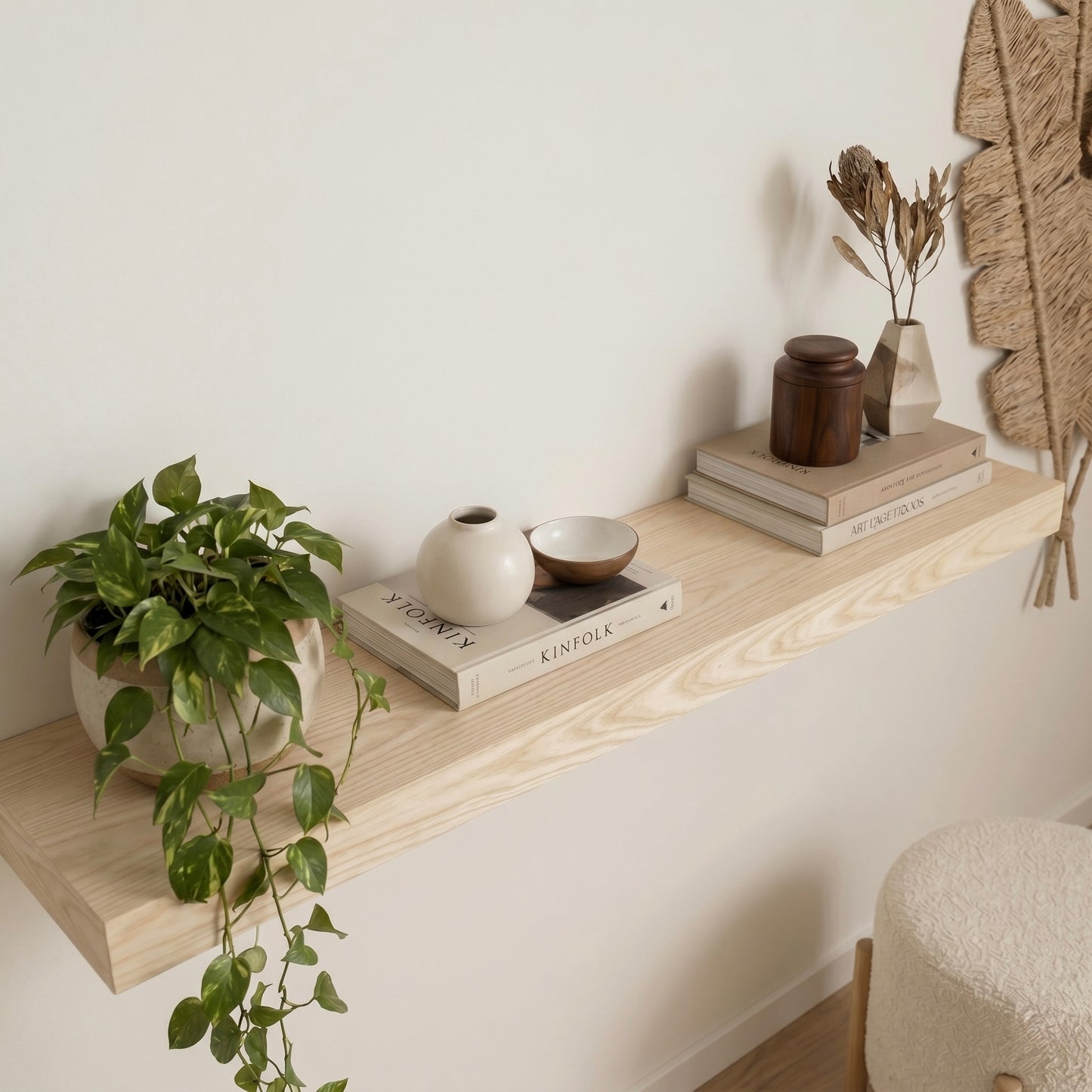 Nahaufnahme eines schwebenden Wandregals aus Esche mit natürlicher Holzmaserung. Dekoriert mit Zimmerpflanze, Büchern und Keramikvasen an einer hellen Wand im modernen Wohnzimmer.