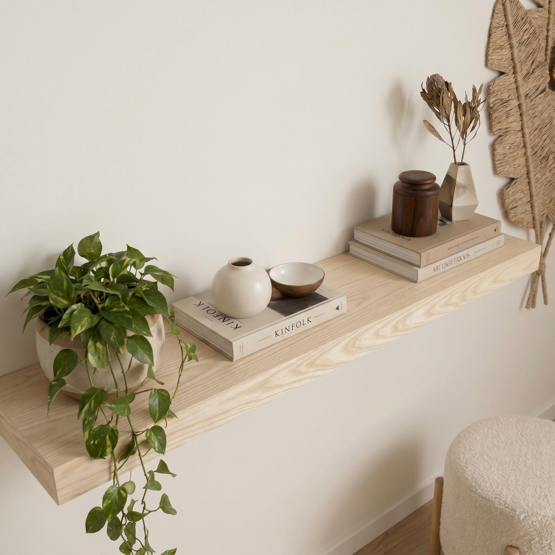 Nahaufnahme eines schwebenden Wandregals aus Esche mit natürlicher Holzmaserung. Dekoriert mit Zimmerpflanze, Büchern und Keramikvasen an einer hellen Wand im modernen Wohnzimmer.