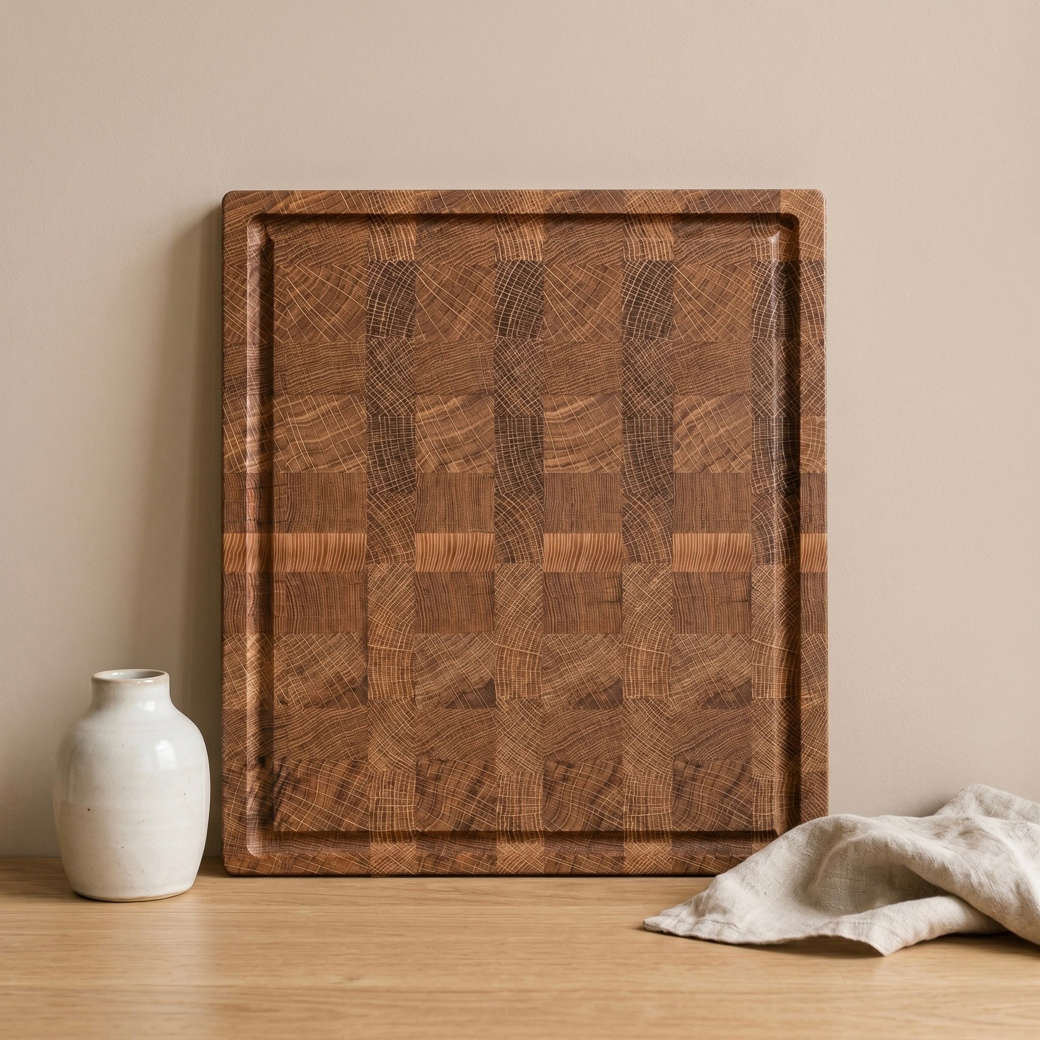 Massives Stirnholz-Schneidebrett aus Eiche mit markanter Endgrain-Maserung und Saftrille. Minimalistische Szene mit heller Keramikvase und Leinentuch.