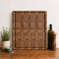 Massives Stirnholz-Schneidebrett aus Eiche mit markanter Endgrain-Maserung und Saftrille. Frontal aufgenommen in heller Küche mit Ölflasche und Gewürzmühle.