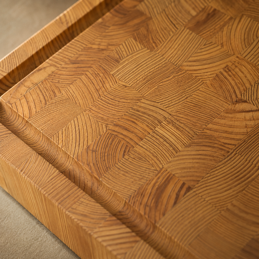 Nahaufnahme eines Stirnholz-Schneidebretts aus Lärche mit markanter Endgrain-Maserung und eingefräster Saftrille. Die warme Holzfarbe und die feinen Jahresringe sorgen für eine hochwertige, handwerkliche Optik.