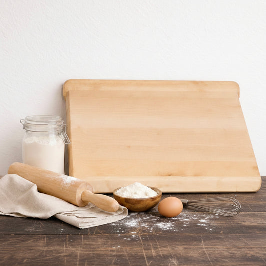 Massives Backbrett aus Ahorn mit Mehl, Ei und Backutensilien auf Holzarbeitsfläche