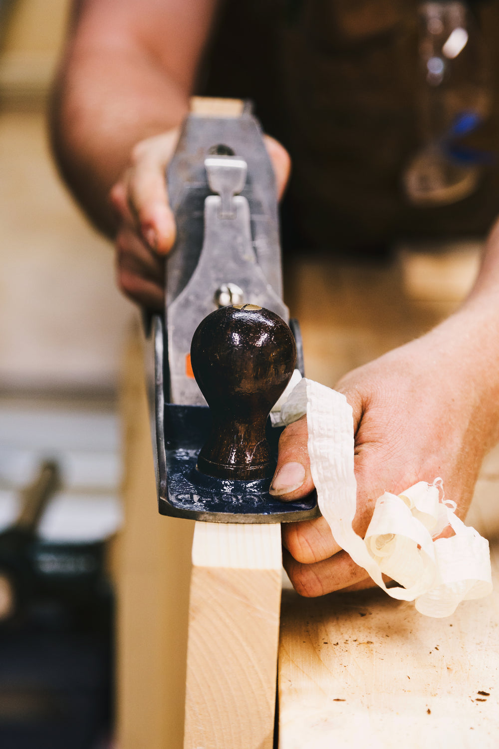 Schreiner hobelt Holz mit Handhobel, feine Holzspäne entstehen in der Werkstatt