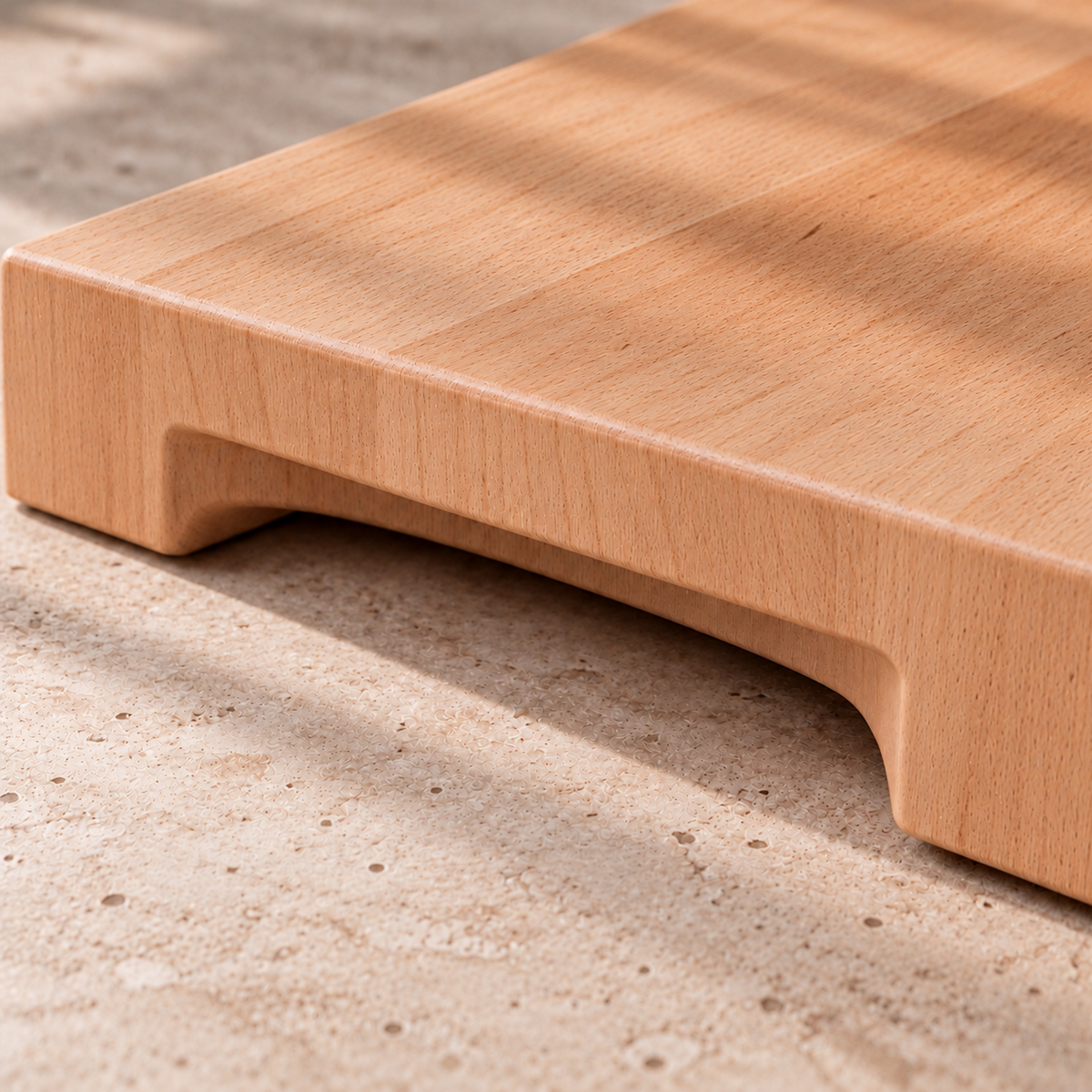 Detailaufnahme eines massiven Schneidebretts aus Buche mit eingefräster Griffmulde an der Unterseite und glatt geschliffener Holzkante.