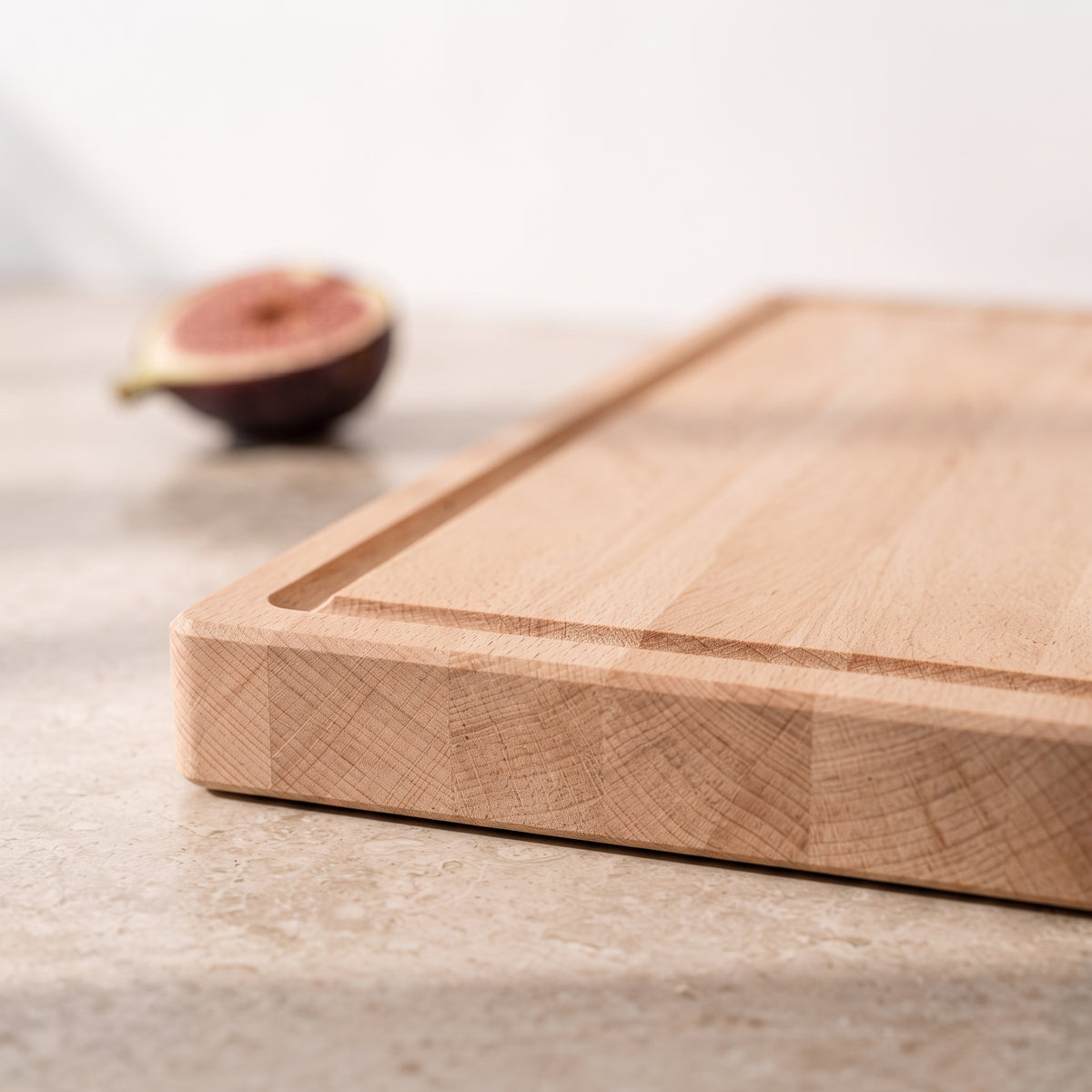 Nahaufnahme eines Schneidebretts aus Buche mit eingefräster Saftrille, massiver Holzkante und fein gemaserter Oberfläche.