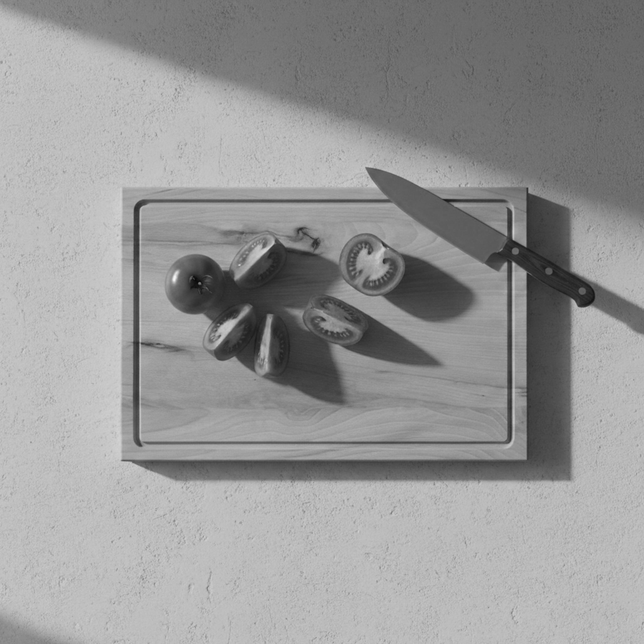 Schneidebrett aus Buche mit Saftrille, Tomaten und Küchenmesser im seitlichen Licht von oben fotografiert