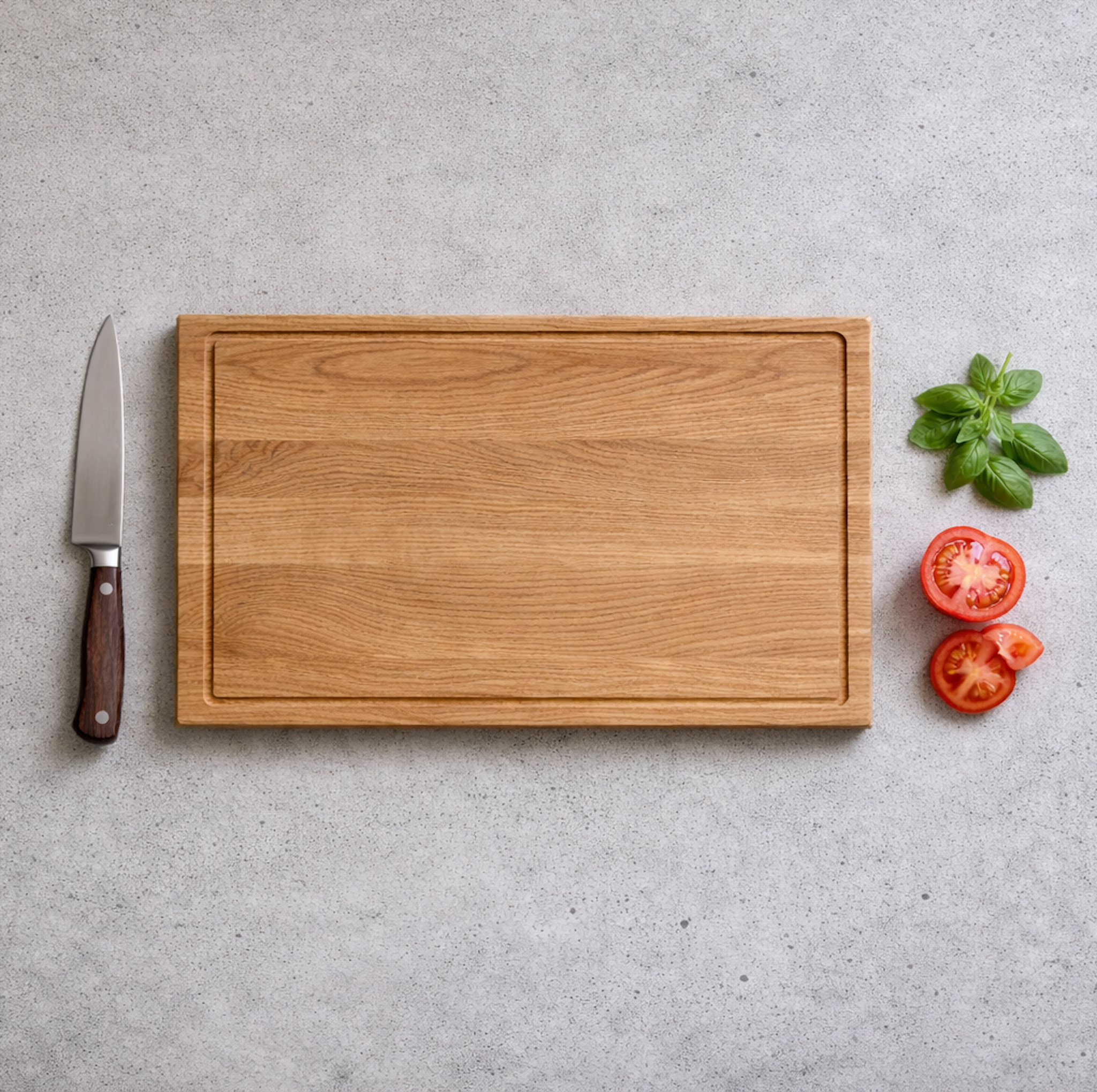 Schneidebrett aus massiver Eiche mit Saftrille in Draufsicht, daneben Messer, Tomaten und Basilikum