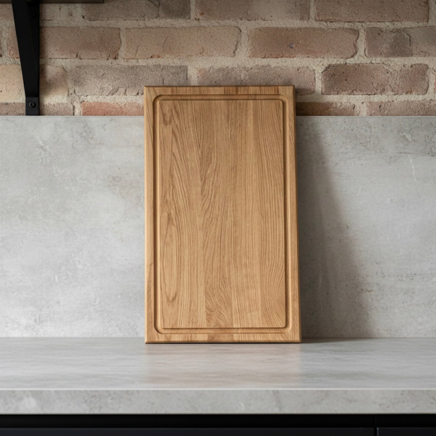 Handgefertigtes Schneidebrett aus massiver Eiche mit Saftrille, stehend auf heller Arbeitsfläche vor Ziegelwand