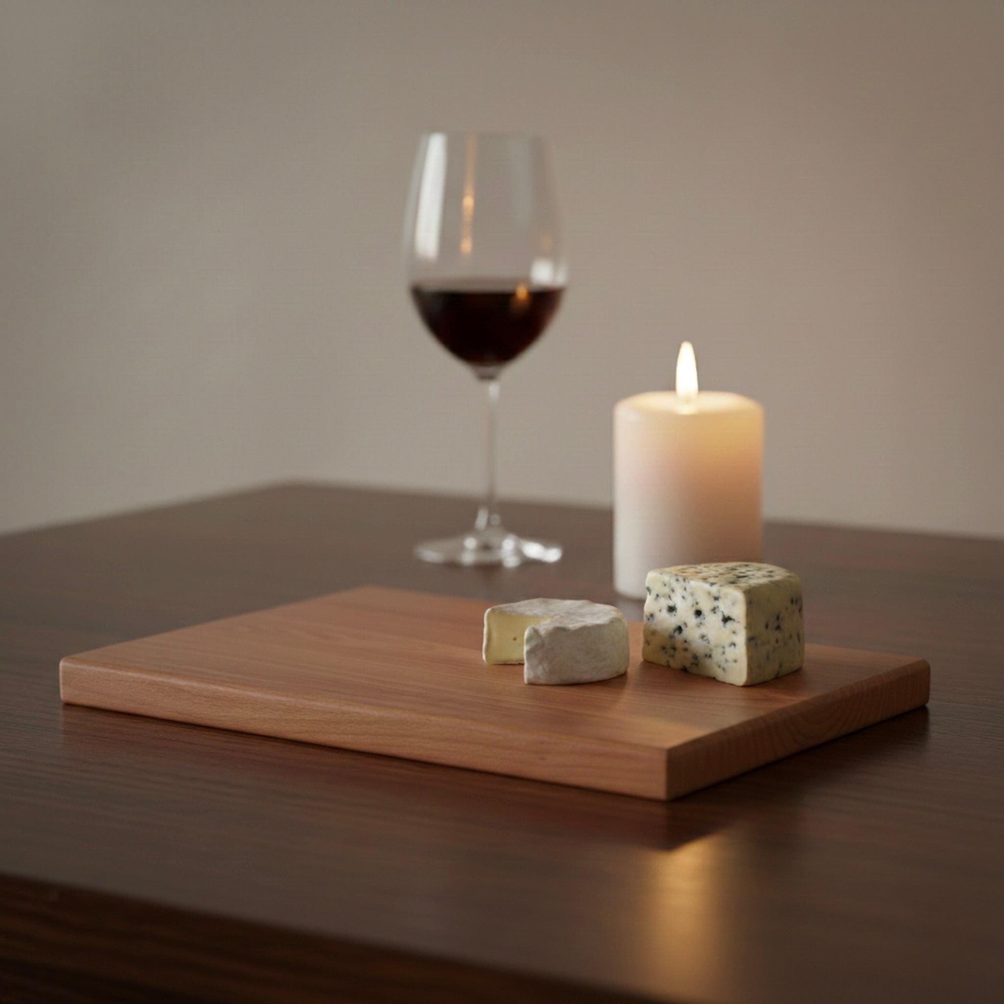 Schneidebrett aus massivem Kirschbaum mit Käse, Weinglas und Kerze in Abendstimmung
