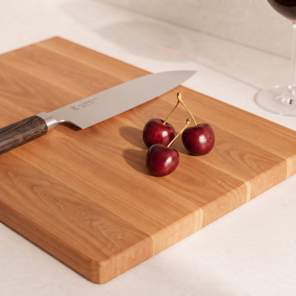 Massives Schneidebrett aus Kirschholz mit natürlicher Holzmaserung, darauf frische Kirschen und ein Küchenmesser mit Holzgriff.