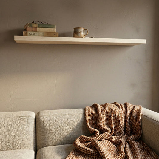 Schwebendes Wandregal aus Ahorn furniert über einem Sofa mit Büchern und Tasse in einem warmen, gemütlichen Wohnzimmer