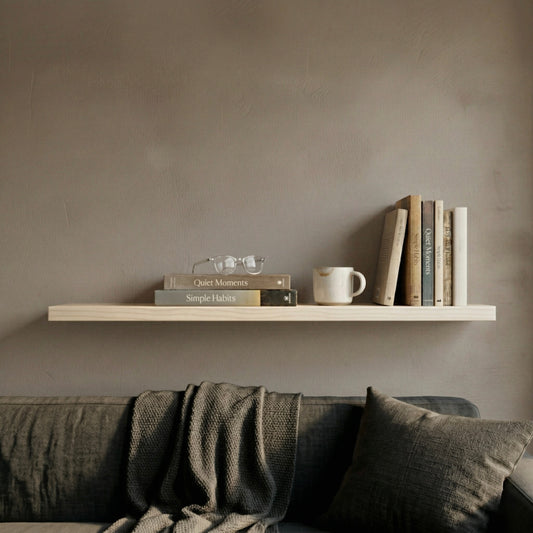 Schwebendes Wandregal aus Ahorn mit Büchern und Tasse über einem Sofa in ruhigem, hellem Wohnambiente