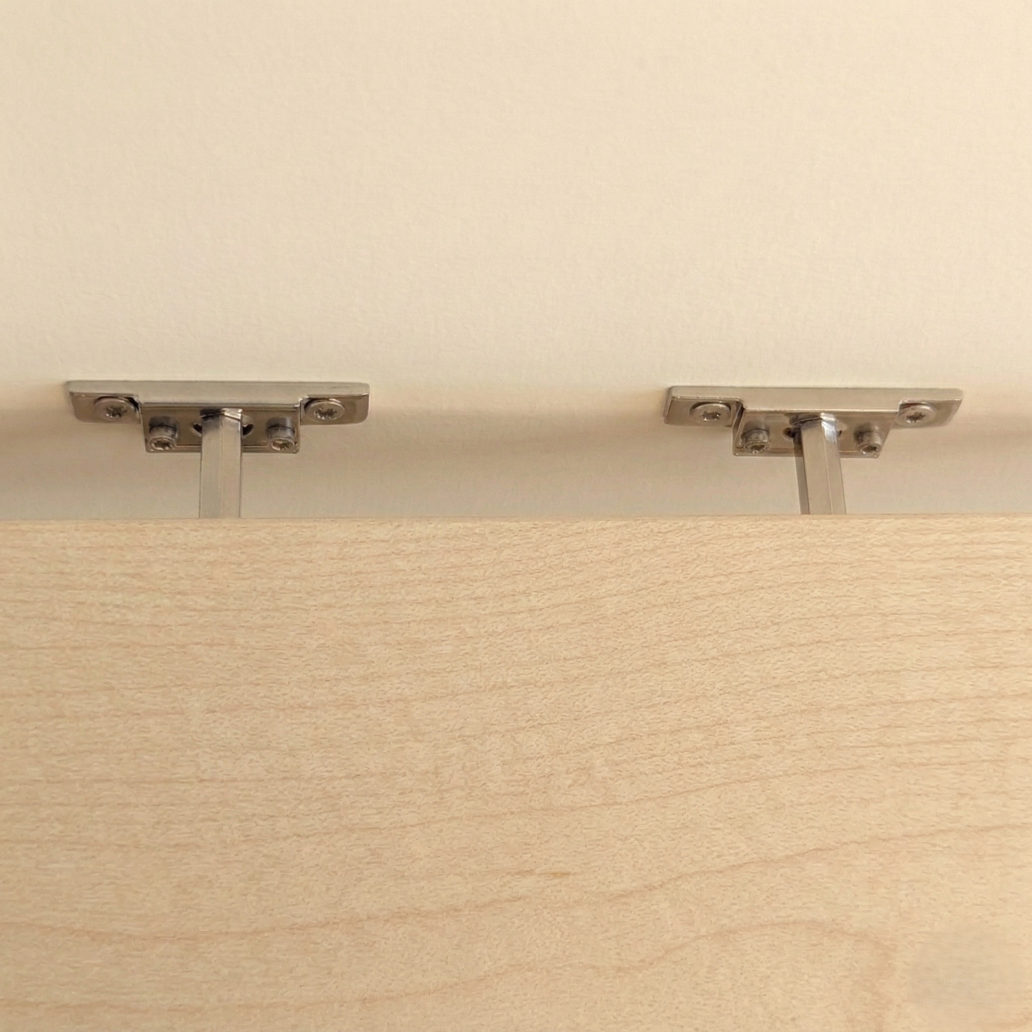 Detailaufnahme der verdeckten Befestigung eines schwebenden Wandregals aus Birke mit Metallhalterungen an der Wand
