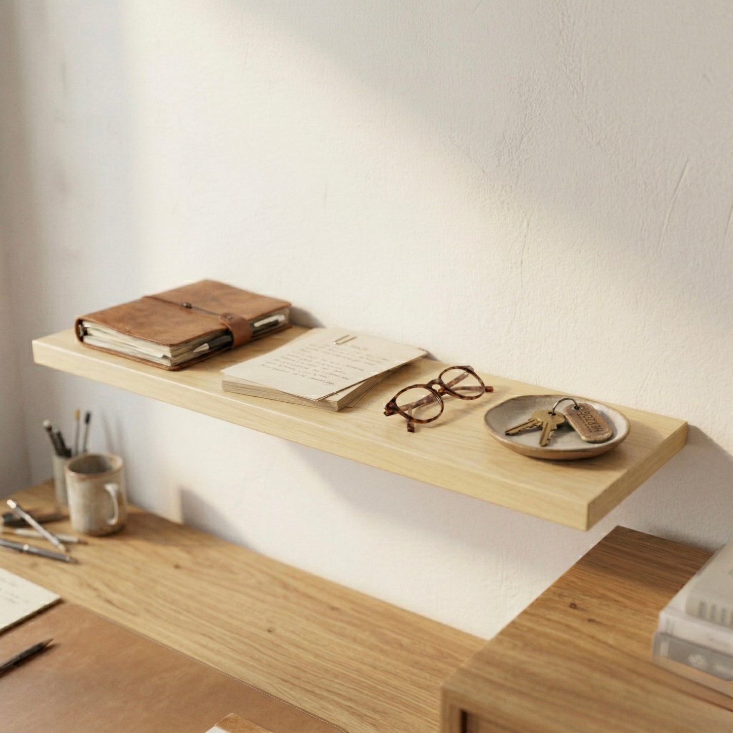 Schwebendes Wandregal aus Birke furniert über einem Schreibtisch mit Notizbuch, Brille und Schlüssel in einem warmen, minimalistischen Arbeitsbereich