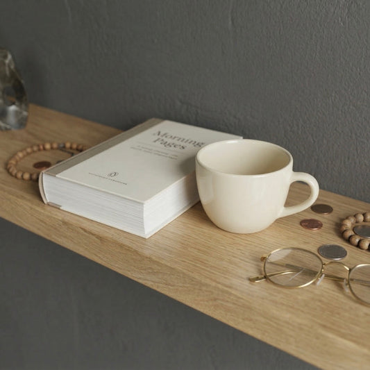 Detailaufnahme eines schwebenden Wandregals aus massiver Eiche mit Buch, Tasse und persönlichen Gegenständen