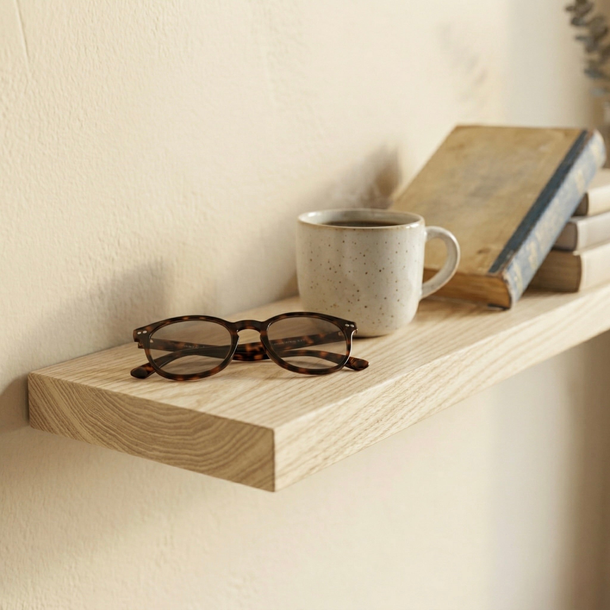 Detailaufnahme eines schwebenden Wandregals aus Esche Massivholz mit Brille, Keramiktasse und Büchern in warmer, minimalistischer Umgebung