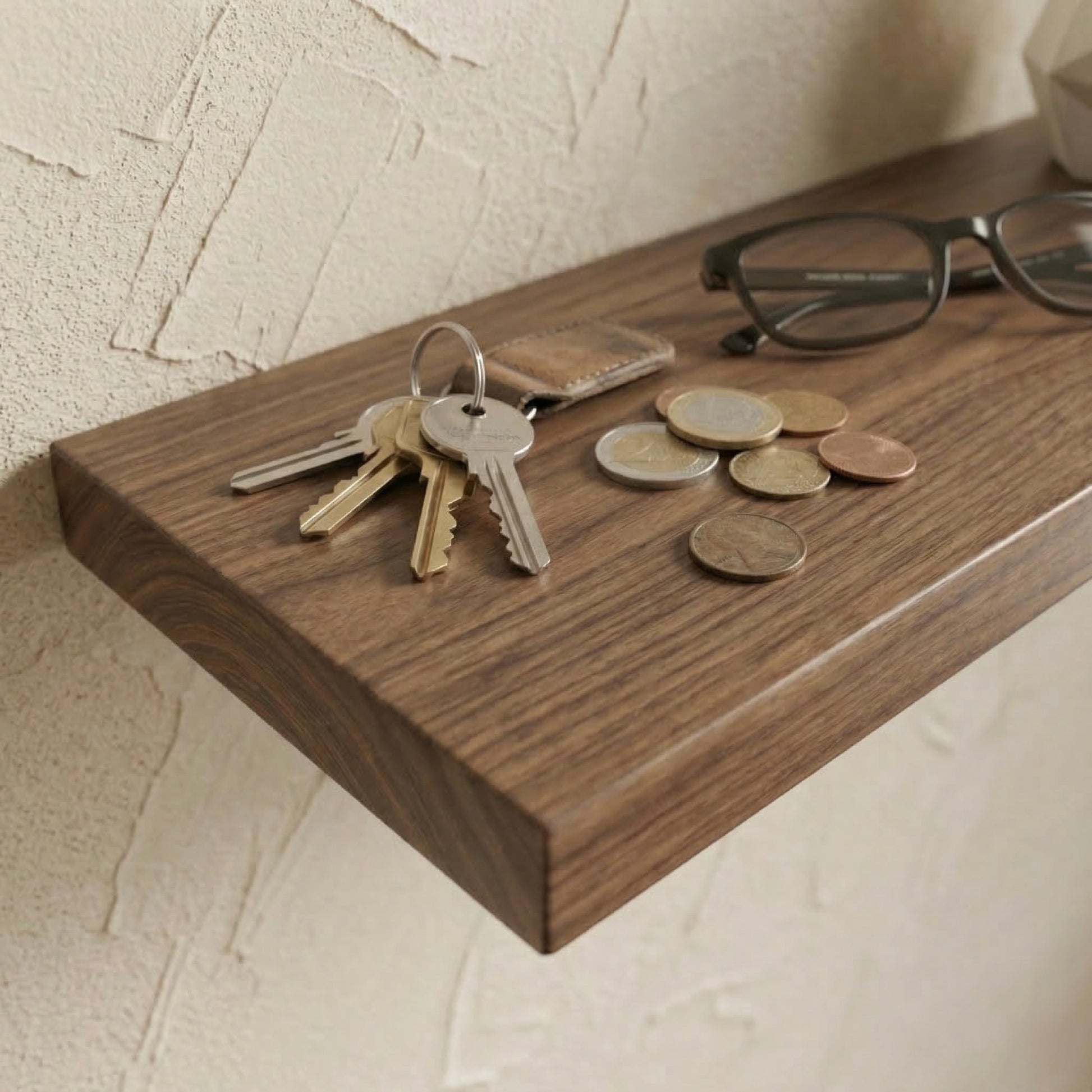 Detailaufnahme eines schwebenden Wandregals aus Nussbaum furniert mit Schlüsseln, Münzen und Brille auf der Holzoberfläche